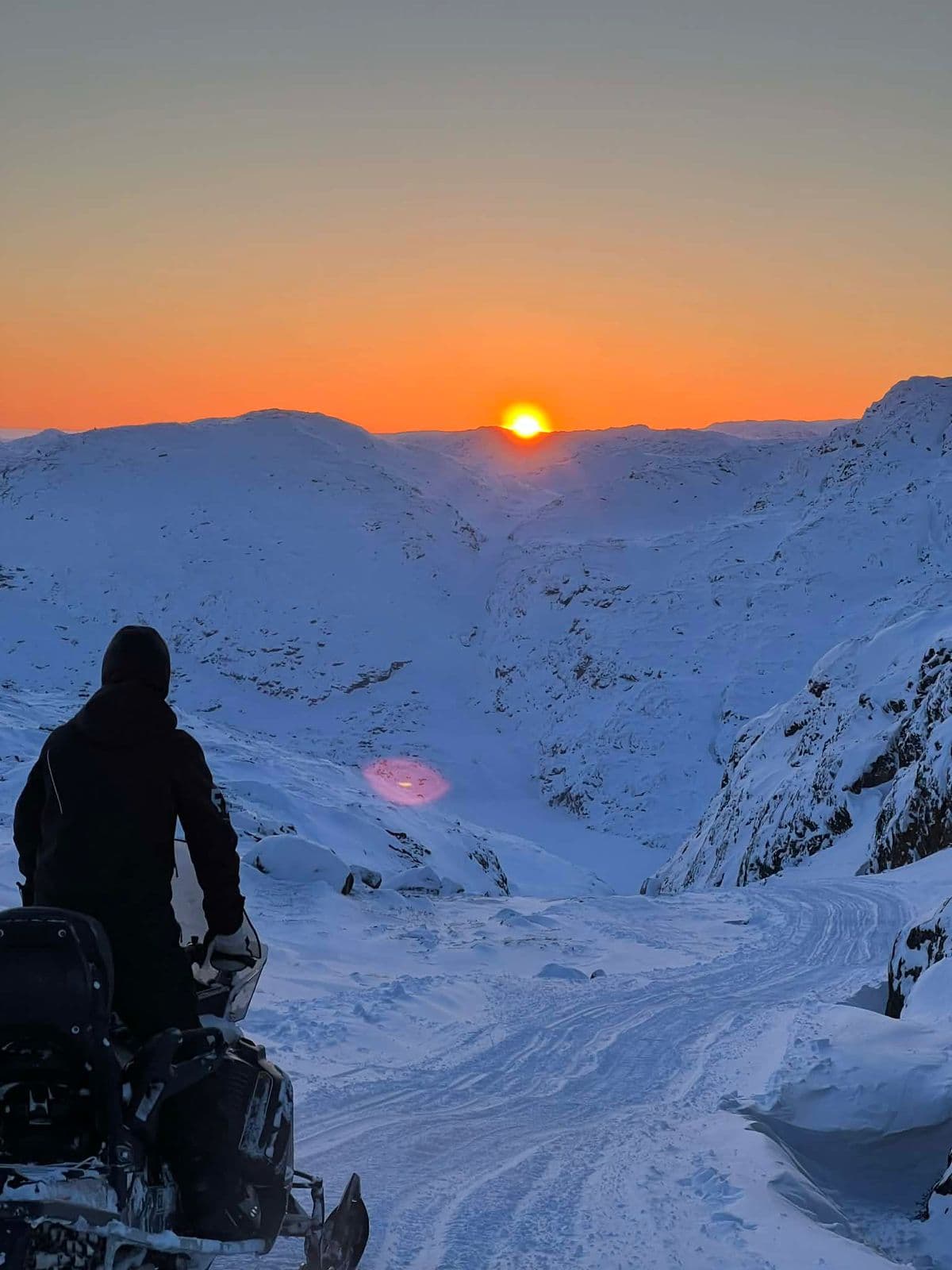 A snowmobile rider at sunset over the icefjord